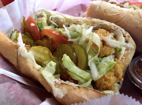 A close-up of a sandwich filled with lettuce, tomatoes, pickles, and crispy fried pieces in a soft bun.