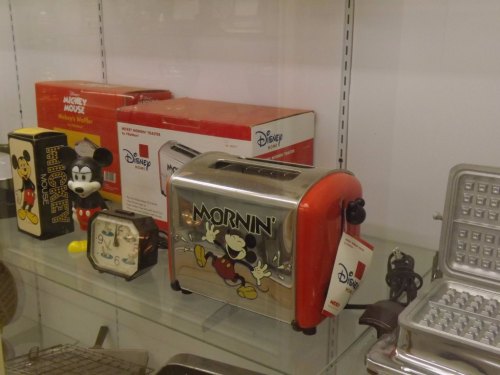 A vintage Mickey Mouse toaster and clock displayed in a glass case, featuring colorful Disney branding.