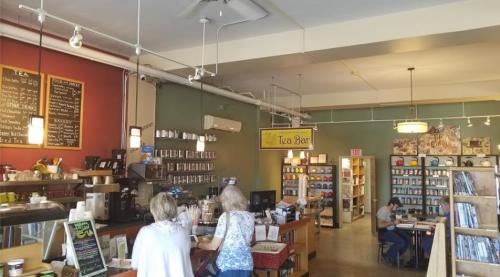 A cozy tea bar with shelves of tea, a counter, and customers enjoying the space. Warm colors and a welcoming atmosphere.