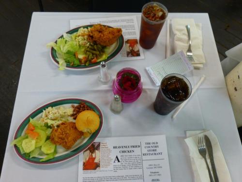 A table set with two plates of fried chicken, sides, drinks, and menus at a restaurant.
