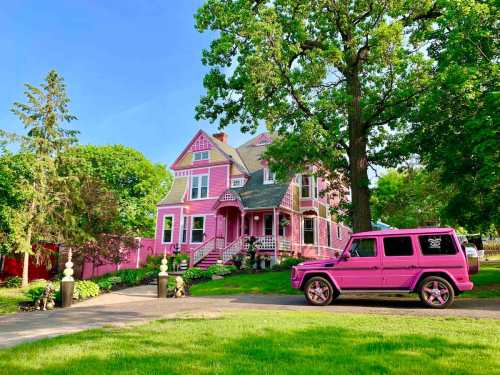 A vibrant pink house with a matching pink SUV parked in front, surrounded by lush greenery and trees.