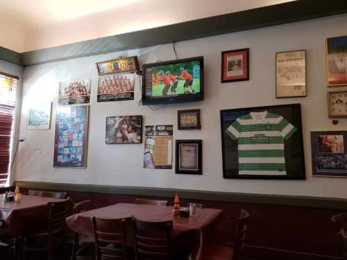 Interior of a restaurant with tables, a TV showing sports, and walls decorated with framed photos and memorabilia.