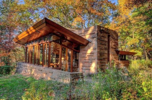 A modern wooden house surrounded by colorful autumn trees, featuring large windows and a unique architectural design.