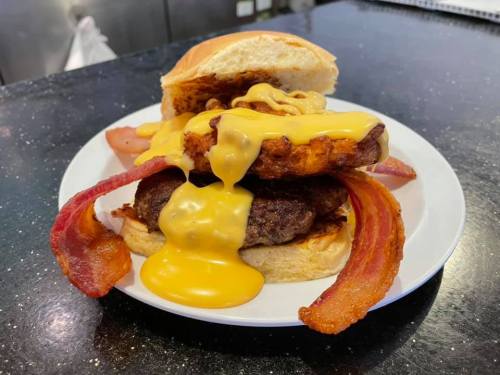 A stacked burger with melted cheese, crispy bacon, and a toasted bun, served on a white plate.
