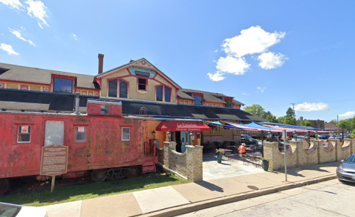 A historic building featuring a red train car, outdoor seating, and colorful architecture under a clear blue sky.