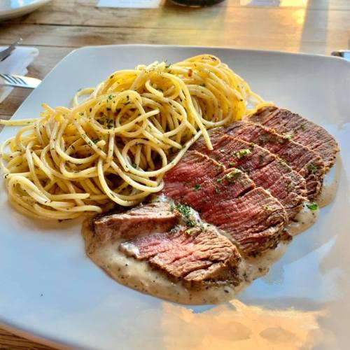 A plate featuring sliced beef with creamy sauce, served alongside a portion of spaghetti.