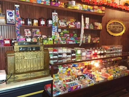 A vintage candy store display featuring jars of sweets, boxes of candy, and an antique cash register.