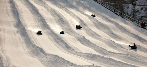 A snowy slope with several people sledding down on colorful tubes, creating tracks in the fresh snow.