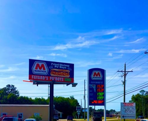 Billboard advertising Fayard's Po'Boys with fried shrimp, alongside a gas station price sign showing fuel prices.
