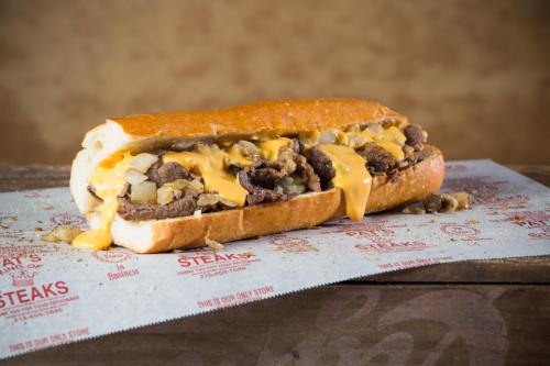 A loaded cheesesteak sandwich with beef, onions, and melted cheese on a toasted hoagie roll, served on paper.