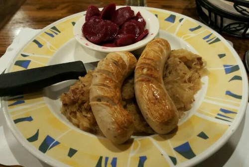 Plate of two grilled sausages on sauerkraut, served with a side of pickled beets in a small bowl.