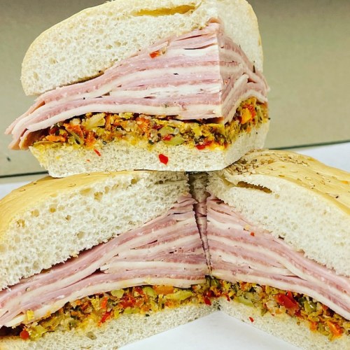 A close-up of a sandwich cut in half, featuring layers of ham and a colorful vegetable spread on sesame seed bread.