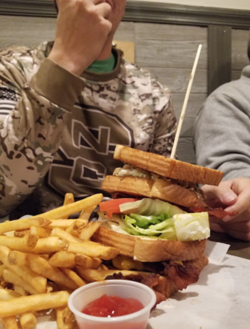 A towering sandwich with layers of ingredients, served with a side of fries and a small cup of ketchup.