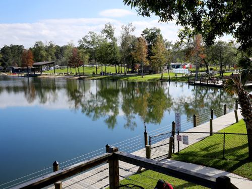 A serene lake surrounded by trees, with a wooden dock and grassy areas under a clear blue sky.