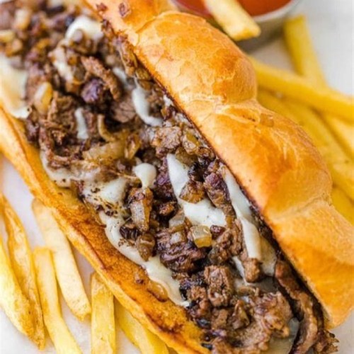 A loaded sandwich with beef, onions, and melted cheese, served with crispy French fries on the side.