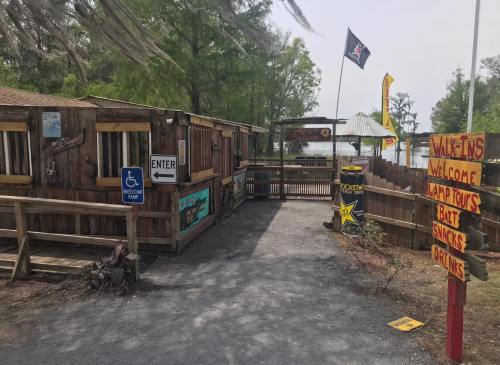 Rustic entrance to a lakeside shack with signs for snacks and drinks, surrounded by trees and a welcoming atmosphere.