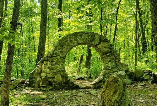A stone archway surrounded by lush green trees in a serene forest setting.