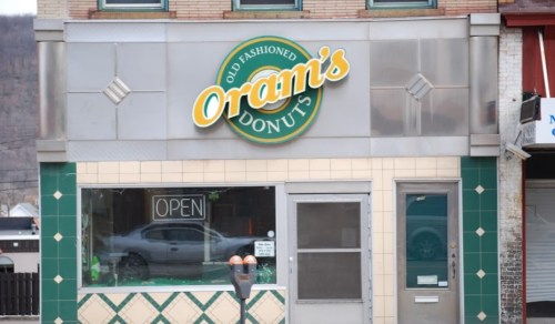 Sign for Oram's Donuts, featuring "Old Fashioned Donuts" with an open window and a green and white tiled exterior.
