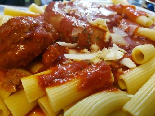 A close-up of pasta with meatballs and sausage, topped with marinara sauce and grated cheese.