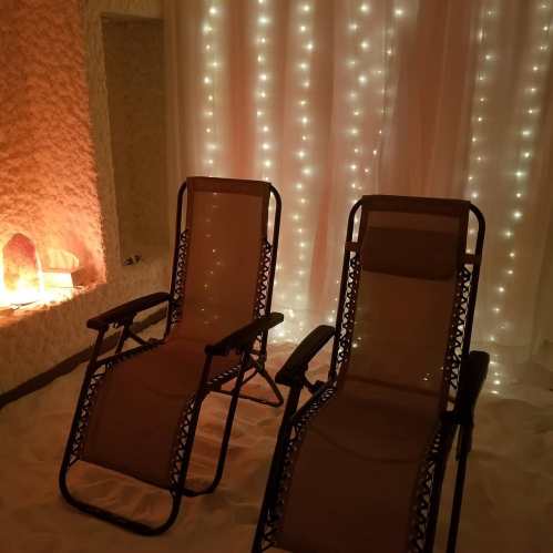 Two lounge chairs in a serene room with soft lighting and a salt wall, creating a relaxing atmosphere.