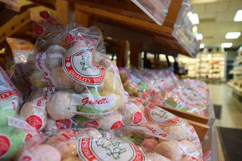 Bags of colorful, fresh pastries displayed on wooden shelves in a bakery.