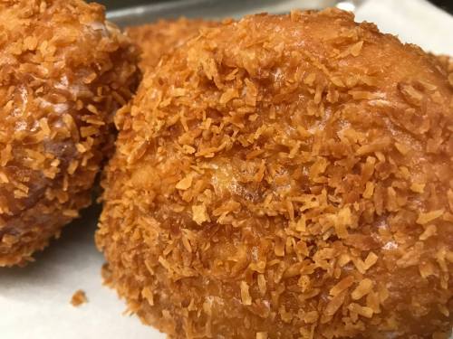 Close-up of golden-brown, crispy fried dough balls coated in crunchy flakes on a white surface.