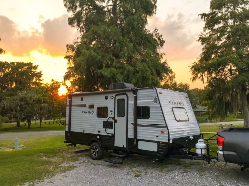 A Viking travel trailer parked on gravel, with a sunset and trees in the background.