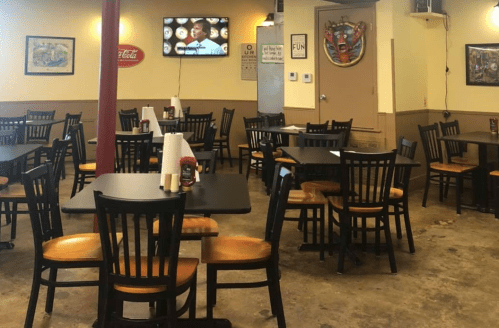 A casual dining area with black tables and chairs, featuring a TV and decor on the walls.