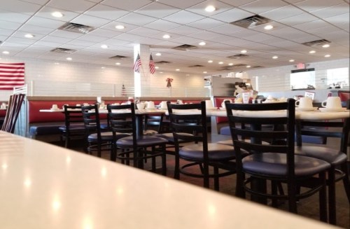 A diner interior with empty booths, tables set for dining, and American flags decor. Brightly lit and inviting atmosphere.