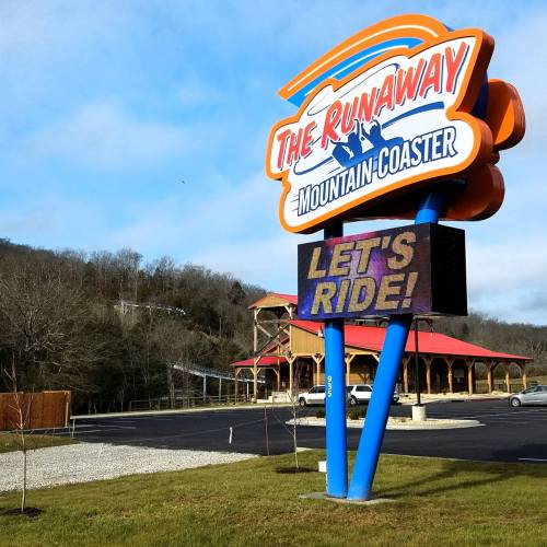 Sign for "The Runaway Mountain Coaster" with a bright display reading "LET'S RIDE!" in a scenic outdoor setting.