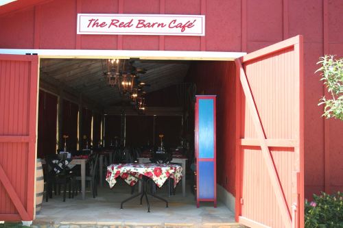 Entrance to The Red Barn Café, featuring tables with floral tablecloths and rustic decor inside a red barn.