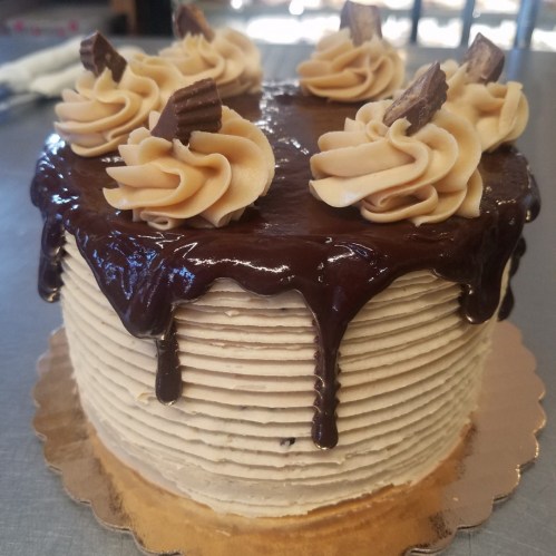 A round cake with chocolate ganache, peanut butter frosting, and topped with swirls and chocolate pieces.