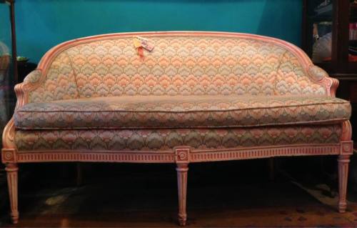 Antique sofa with a floral pattern and ornate wooden legs, set against a vibrant blue wall.