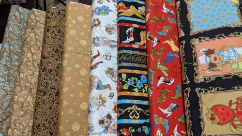 A variety of colorful fabric rolls featuring patterns like flowers, cowboys, and decorative designs.