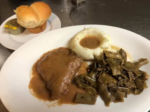 A plate with beef in gravy, mashed potatoes, green beans, and a side of two dinner rolls.