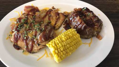 Grilled chicken topped with cheese and bacon, served with a baked potato and corn on the cob.
