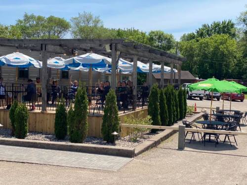 Outdoor dining area with umbrellas, surrounded by greenery, and people enjoying their meals on a sunny day.