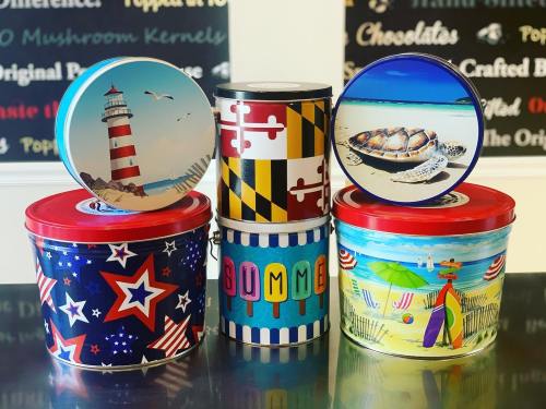 A collection of colorful popcorn tins featuring various designs, including a lighthouse, turtle, and summer themes.