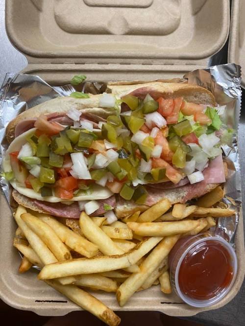 A sandwich loaded with ham, cheese, lettuce, tomatoes, and pickles, served with a side of fries and ketchup.
