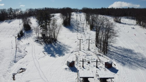 A snowy ski slope with chairlifts and trees under a clear blue sky. Shadows cast on the pristine white snow.