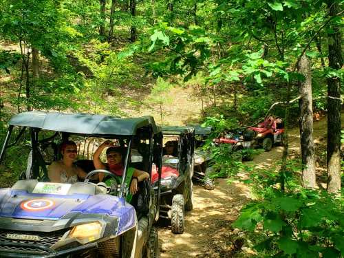 A group of people enjoying an off-road adventure in ATVs on a wooded trail.