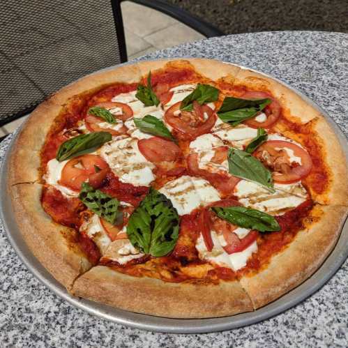 A freshly baked pizza topped with mozzarella, tomatoes, and fresh basil on a stone table.