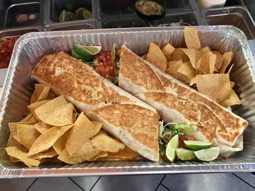 Two large burritos with crispy tortilla chips and lime wedges in a silver takeout tray.