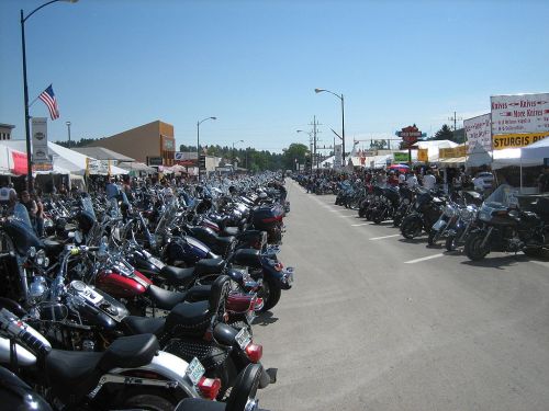 A bustling street lined with rows of motorcycles and vendor tents during a motorcycle rally on a sunny day.