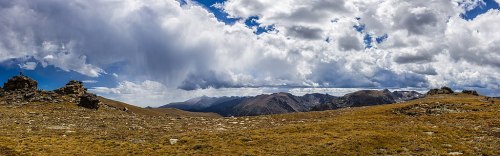 A panoramic view of a mountainous landscape with rocky outcrops and dramatic clouds in a blue sky.