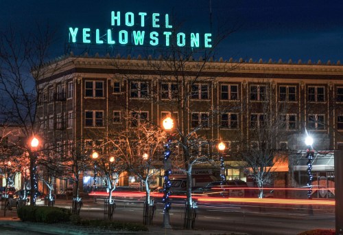 Historic Hotel Yellowstone illuminated at night, with light trails from passing cars and trees adorned with lights.