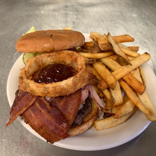 A hearty burger topped with bacon and an onion ring, served with a side of golden French fries.
