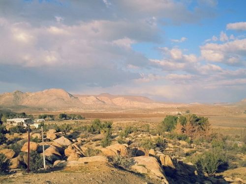 A scenic view of mountains and rocky terrain under a partly cloudy sky, with sparse vegetation in the foreground.