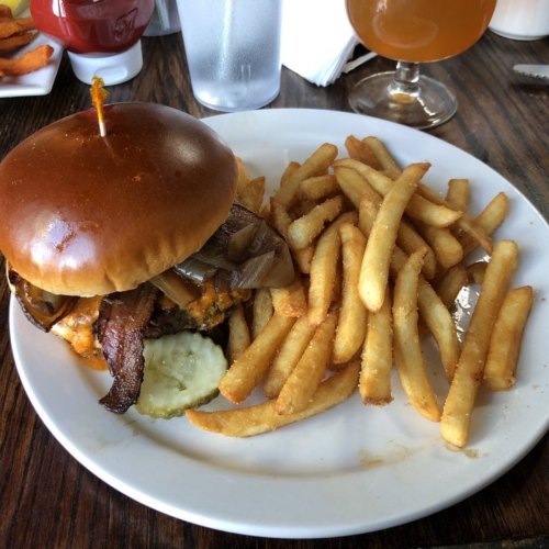 A juicy burger with bacon and onions, served with crispy fries on a white plate.