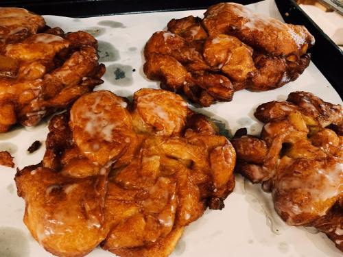 Four golden-brown apple fritters drizzled with a sweet glaze on a parchment-lined baking tray.
